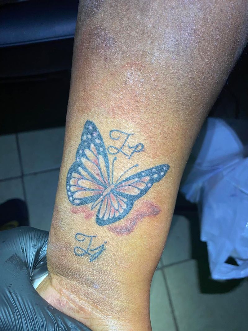 Blue and white butterfly tattoo with small script initials above and below, on an arm.